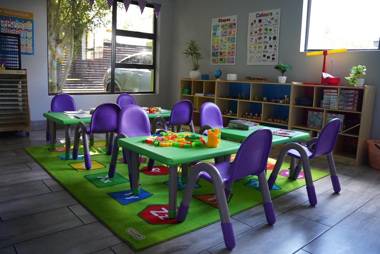 A bright Hibiscus classroom on Rivier Street with green tables, purple chairs and an alphabet rug