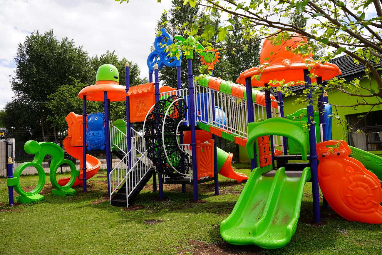 Orange, blue and green jungle gym with slides on the lawn at the Hibiscus Rivier Street campus